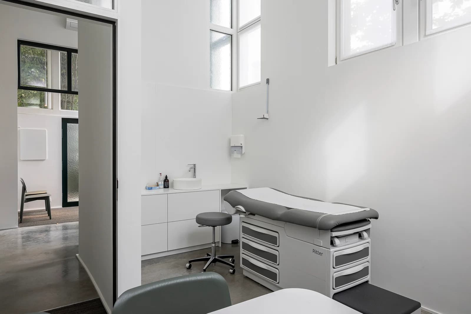 Een consultatieruimte met onderzoekstafel en hoge ramen